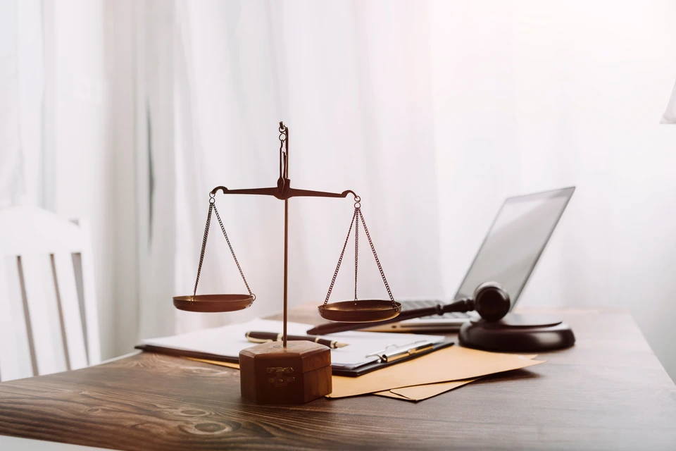 Bureau d'avocat moderne avec balance de justice en laiton au premier plan, marteau de juge et ordinateur portable sur table en bois