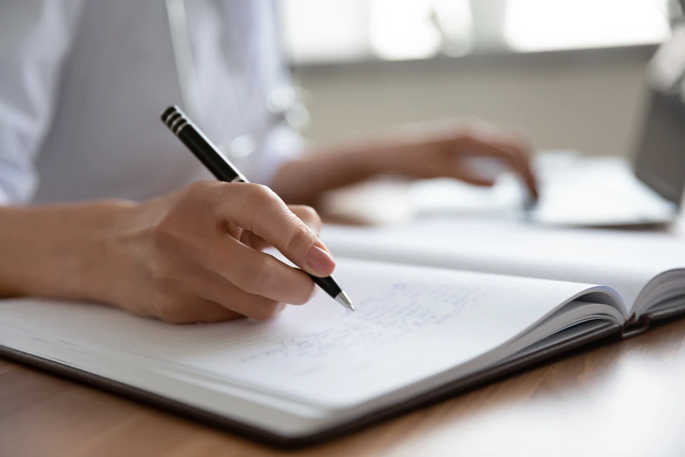 Gros plan sur une femme médecin remplissant des documents et utilisant un ordinateur portable, assise au bureau à l'hôpital, jeune femme médecin thérapeute praticienne gp écrivant l'historique de la maladie, prescription sur une carte de patient