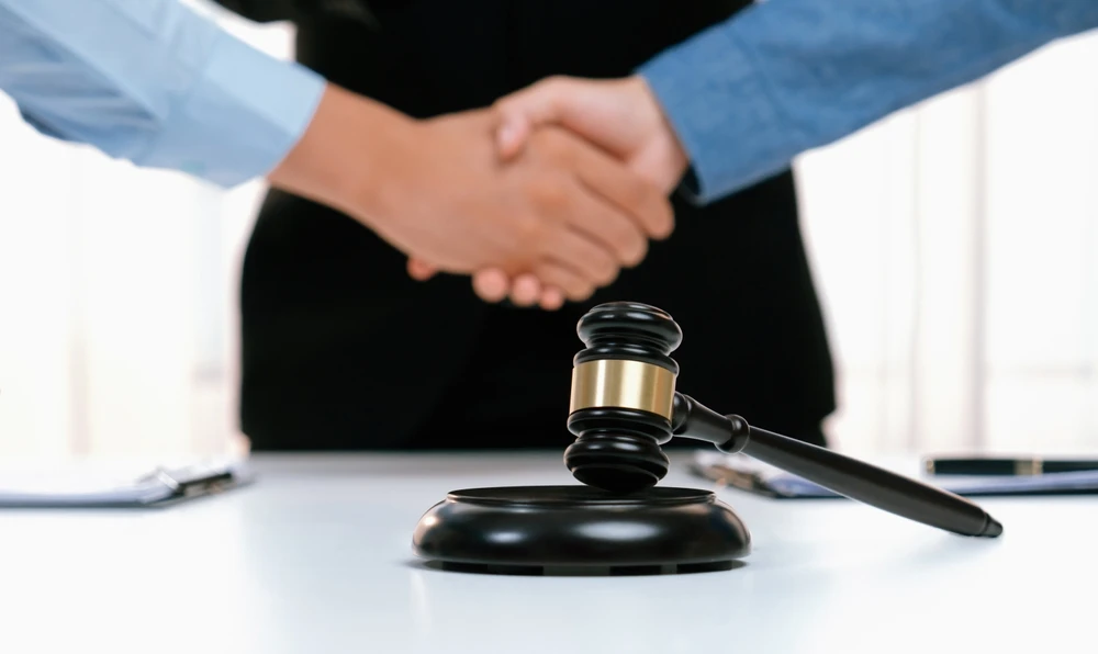 Scène d'intérieur juridique avec personne en robe d'avocat noire à bandes rouges tenant un livre relié rouge