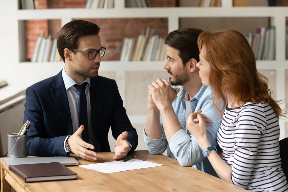 Scène d'intérieur professionnel avec deux personnes en costume se serrant la main au-dessus d'une table, symbolisant un accord juridique ou commercial